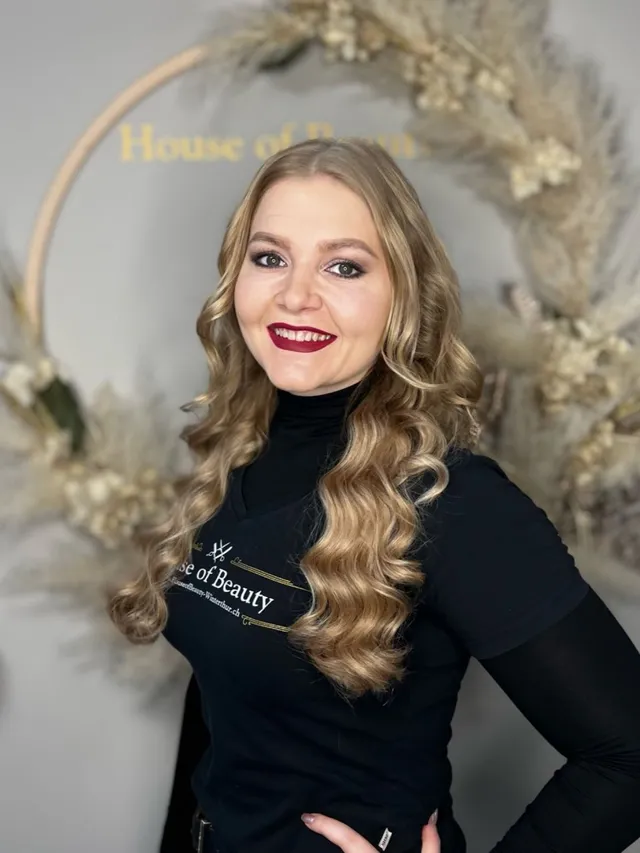 Teammitglied im House of Beauty vor goldenem Dekorreif